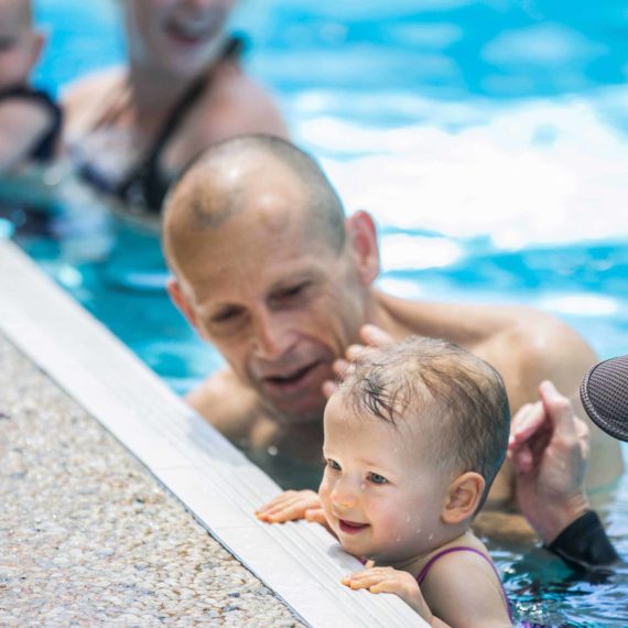 Father teaching baby pool safety with Gina instructing